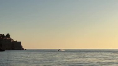 Tekne gölün sakin, sıvı yüzeyinde yüzüyor, alaca karanlık gökyüzü ufuk çizgisiyle buluşurken ve yumuşak rüzgar dalgaları sakin bir manzara yaratıyor.