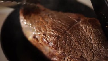 Şef, kızartma için bifteği spatulayla eziyor ve maşayla tavaya vuruyor. Yüksek kalite 4k görüntü