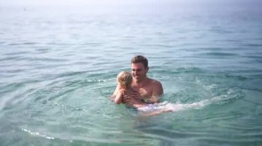Babası küçük bir çocuğa karnını tutarak denizde yüzmeyi öğretiyor. Yüksek kalite 4k görüntü