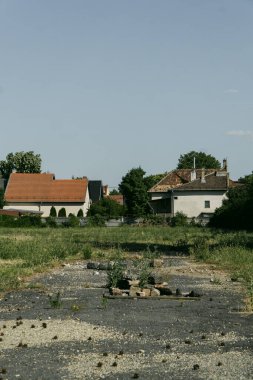 a concrete road with some grass and vegetation behind it with houses on a sunny day
