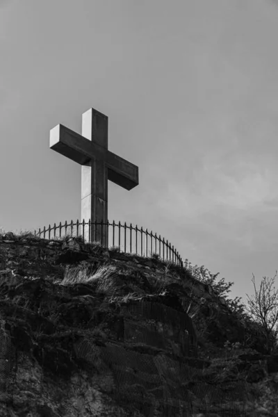 on top of a hill a cross in black and white photographed in budapest vertically with vegetation