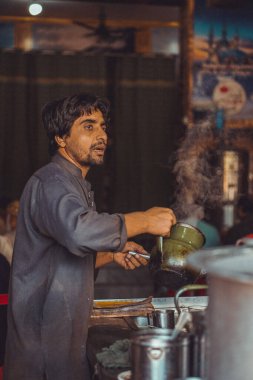 Pakistanlı yemek satıcısı yol kenarındaki yemek standında çaydanlıkta sıcak masala çayı hazırlıyor.