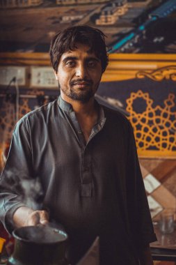 Portrait of a Pakistani man, food vendor holding a chai, the local tea kettle in his roadside street tea stall clipart