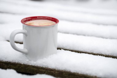 A cup of hot drink on a snowy wooden pallet. winter.
