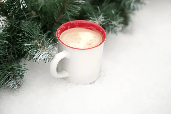 a mug of coffee on the snow near a coniferous garland.