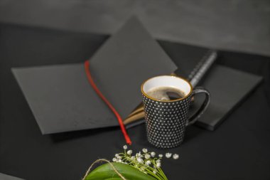 Siyah arka planda açık bir not defteri, bir fincan kahve ve zambaklar..