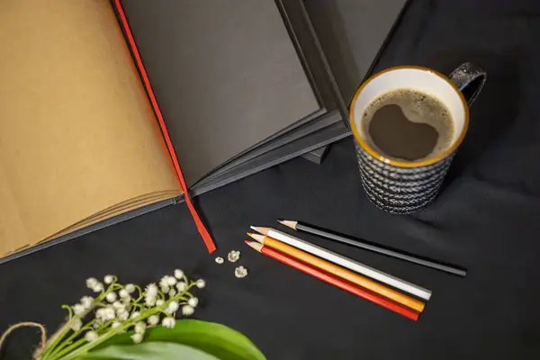 notepad, pencils, a cup of coffee, lilies of the valley on a black background.