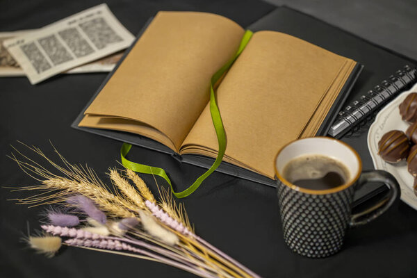 notepad, chocolates, a cup of coffee, old flyers and spikelets on a black background.