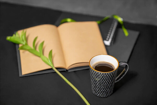 notebooks, a sketchbook, a cup of coffee, a green twig on a black background.