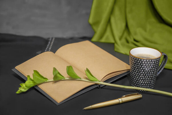 notebooks, sketchbook, cup of coffee, gold pen, green branch on black background.