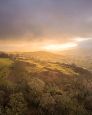 Sunrise over Denbighshire hills, Wales, as the sun breaks through dark clouds and light rain falls upon the countryside clipart