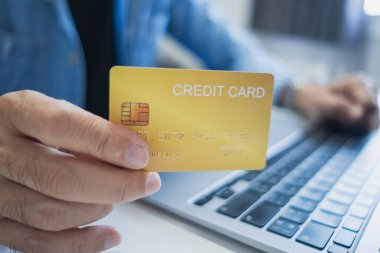 Kapat, Adam dizüstü bilgisayar kullanırken kredi kartı tutuyor, internetten alışveriş yapıyor, internetten alışveriş yapıyor. E-ticaret e-bankacılık servisi. Bilgisayarda çalışan başarılı bir serbest yazar. Çevrimiçi güvenli ödeme.