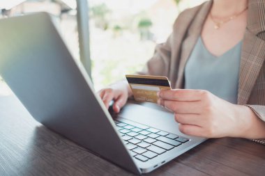 Kredi kartı tutan bir kadın, laptopunu ve açık havada kahve dükkanında alışveriş yaparken, internet bankacılığı, e-ticaret e-bankacılık hizmetleri. Bilgisayarda çalışan başarılı bir serbest yazar. Çevrimiçi güvenli ödeme.