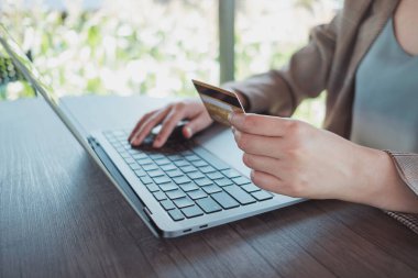 Kredi kartı tutan bir kadın, laptopunu ve açık havada kahve dükkanında alışveriş yaparken, internet bankacılığı, e-ticaret e-bankacılık hizmetleri. Bilgisayarda çalışan başarılı bir serbest yazar. Çevrimiçi güvenli ödeme.