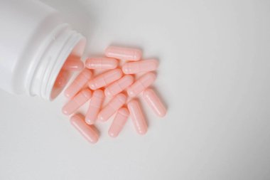 Üzerinde pembe ilaç kapsülleri olan beyaz arka planda fotokopi alanı olan bir şişe kutusu. Güzellik, sağlık, sağlık ve tıp konsepti.