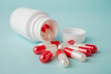 Kırmızı ve beyaz ilaç kapsüllü şişe kaplarını mavi arka planda kapat. Güzellik, sağlık, sağlık ve tıp konsepti.