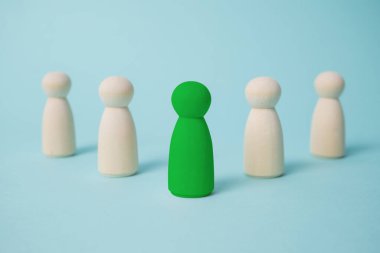 Yeşil, diğerlerini mavi arka plandaki diğer tahta bebeklere yönlendiriyor. Liderlik kavramı. 