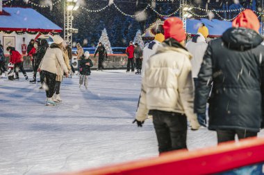 Mutlu aileler, arkadaşlar parkta buz pateni pistinde birlikte kayıyorlar. Şehirde karlı bir akşam. Kış sporu, açık hava aktiviteleri