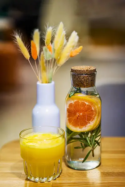Glass of freshly squeezed juice in glass next to bottle with refreshing drink and vase of colorful cereals. Concept of healthy lifestyle and detox