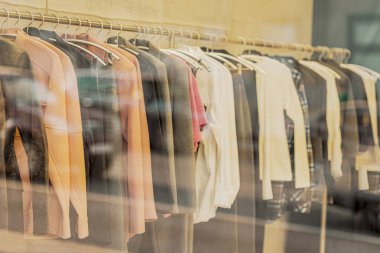 Kadın kıyafetleri raylarda asılı duruyor. Bir depo penceresinden bulanık görünüm, seçici odak