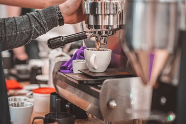 Kahve dükkanında kahve yapan profesyonel baristanın elleri, porselen bardağa taze içecek dolduran kahve makinesi.