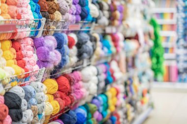 Örgü iplikleriyle dolu rafların soyut arkaplanı bulanık. Mağazada iplik derileri. Hobiler ve dikiş işi. Seçici odak