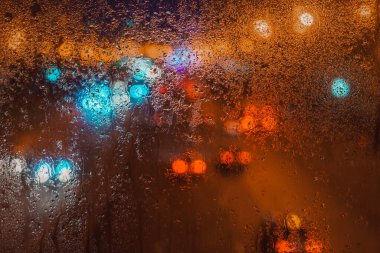 Arka planda bulanık şehir ışıkları olan pencereye yağmur damlaları, soyut gece atmosferi