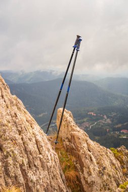 Yürüyüş direkleri sisli bir öğleden sonra arka planda dağ manzarası olan kayalık bir çıkıntıya yaslandı.