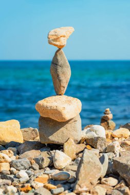 Kayalık bir sahilde dengeli taş yığını, arka planda okyanus ve mavi gökyüzü, uyum kavramı