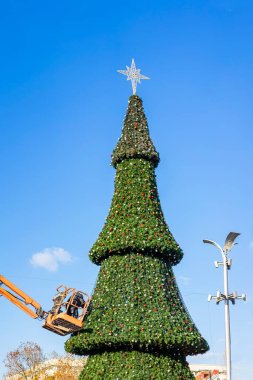 Açık havada, üzerinde yıldız olan açık mavi bir gökyüzünün altında süslenmiş büyük bir Noel ağacı.