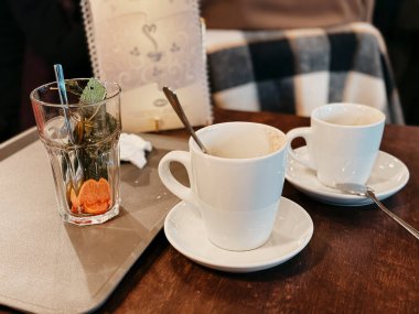 Used glass of tea with mint and citrus slice and empty coffee cups on a table, finishing eating at a cafe clipart