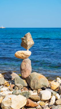 Kayalık bir sahilde özenle dengelenmiş taşlar ve arka planda mavi bir okyanus. Uyum, meditasyon, farkındalık, zen uyumu ve denge konsepti sembolü