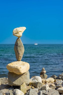 Kaya yığını kıyıda tehlikeli bir şekilde dengelenir. Mavi gökyüzüne karşı çakıl taşı sahilinde dengelenmiş uzun ve narin taş kule. Sabır ve hassasiyeti temsil eder.