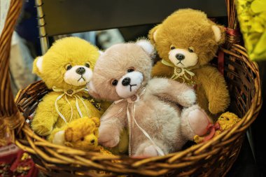 Yumuşak ve renkli oyuncak ayılar, dokuma sepetinde dizilmiş. Boyunlarında kurdelelerle dokuma sepetinde oturan üç pelüş oyuncak ayı. Çocukluk nostaljisi, rahatlık, el yapımı işçilik konsepti