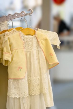 Tahta askıda asılı ince dantelli klasik bir bebek elbisesi. Nostalji anlayışı, çocukluk modası, el yapımı işçilik.