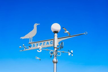 BURGAS, BULGARIA - 21 Mart 2025 Kiril şehri isimli martı şekilli rüzgar gülü, berrak canlı gökyüzü, uçan kuş martıları. Deniz havası, seyahat yönü, açık kıyı bölgesinde sembolik hareket