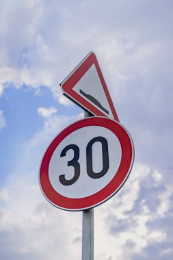 Bulutlu gökyüzünün arka planında 30 km hız sınırı işareti var. Uyarı mesajı. Hız limiti işareti saatte 30 kilometre gösteriyor, ek çarpma uyarısı. Karayolu güvenliği kavramı, dikkat