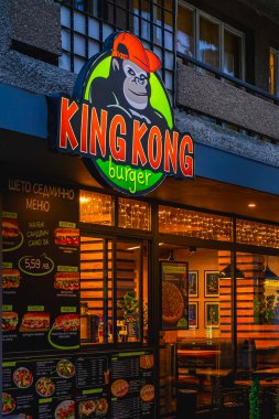 Burgaz, Bulgaristan 'da King Kong Burger sokak yemekleri. Aydınlatılmış goril logosuna sahip hamburger restoranı, akşama doğru renkli bir menü. King Kong Burger yaratıcı markalaşma ve günlük fast food kültürünü somutlaştırıyor.