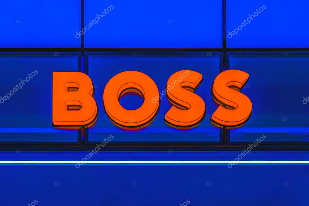 Bright orange BOSS store sign with bold letters on deep blue glass wall in commercial building in Burgas, Bulgaria. BOSS sign conveys fashion brand identity and elegance, retail concept