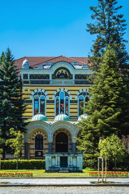 Bulgaristan 'ın Sofya kentindeki Bulgar Ortodoks Kilisesi' nin Kutsal Meclisi. Parlak kilise cephesi ağaçlarla, mavi gökyüzü, kubbeli giriş, kemerli pencereler. Mimarlık geleneği, kültürü, dini inancı yansıtır.