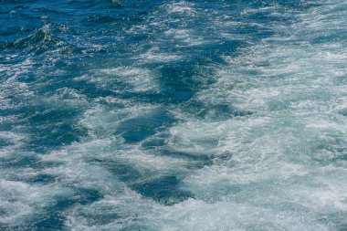 Köpüklü yüzeyi olan mavi okyanus suyu, suyun hareketini ve ışıltısını yakalar. Tazelik ve enerjinin arka planında deniz suyu sahnesi