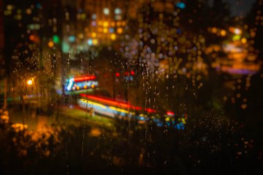 Rengarenk şehir ışıklarıyla kaplı yağmur camları rüya gibi. Yağmur ve bokeh sonbahar havası yaratır. Şehir ışıkları penceredeki yağmur damlalarında bulanıklaşır, şehir manzarasında gece vakti, arka planda canlı bulanıklaşır