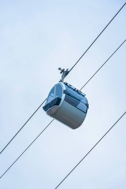 Modern teleferik, yumuşak bulutlu arka planda çelik teller üzerinde gökyüzünde süzülüyor. Kablo taşıma, fütüristik seyahat, yüksek hareketlilik kavramı