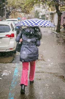 Kar yağarken şemsiyeyle koşuşturan ve ıslak şehir caddesinde yağmur yağan bir kadın. Kentsel kış havası, samimi sokak fotoğrafı. Mevsimler, hava durumu