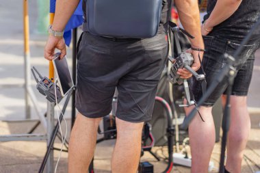 Bir açık hava etkinliğinde insansız hava aracı ve tablet tutan adamlar. İHA operatörleri hava çekimine hazırlanıyor. Video üretimi ve etkinlik kapsamındaki modern teknolojiyi sergiliyorlar.