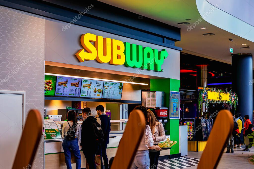 Subway restaurant with bright logo, digital menu boards, and customers waiting to place food orders. Concept of Subway branding, quick service, international fast food