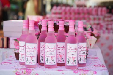 Fuarda bir şişe pembe Rakia. Bulgaristan 'da Gül Festivali. Çiçek masa örtüsüne yerleştirilmiş pembe kapaklı cam gül konyağı şişeleri. Bulgar gül brendisi, çiçek özü ve yerel gelenek kavramı