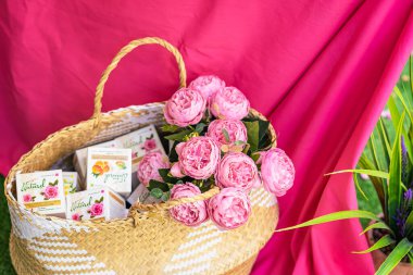 Krem ve güllerle dolu doğal kozmetik kutularla dolu sepet, parlak pembe kumaş arka plan. Doğal cilt bakımı, eko ve çiçek ilhamı kavramı. Rosa damascena. Gül üretim sezonu