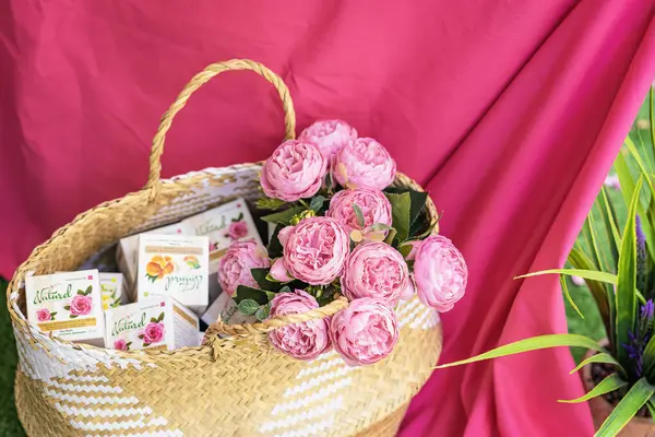 Krem ve güllerle dolu doğal kozmetik kutularla dolu sepet, parlak pembe kumaş arka plan. Doğal cilt bakımı, eko ve çiçek ilhamı kavramı. Rosa damascena. Gül üretim sezonu