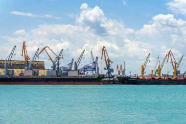 Bulgaristan 'daki kargo limanının panoramik manzarasında bulutlu gökyüzü ve turkuaz su altında birden fazla vinç boşaltılıyor. Küresel ticaret, denizcilik altyapısı, endüstriyel deniz ekonomisi kavramı